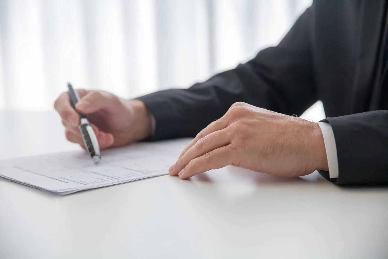 Close-up of a person signing a paper document at a desk, illustrative of paperwork and official forms